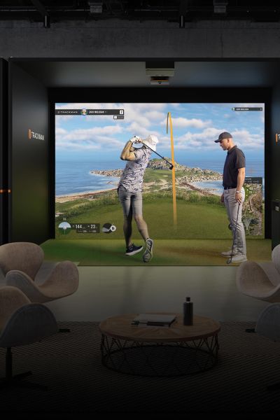 Two men using an indoor golf simulator facing an ocean course projection
