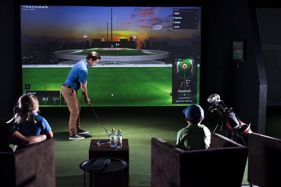 Man lining up a putt on a golf simulator screen while children watch