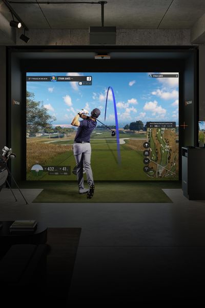 Golfer following through on a swing inside an indoor simulator bay